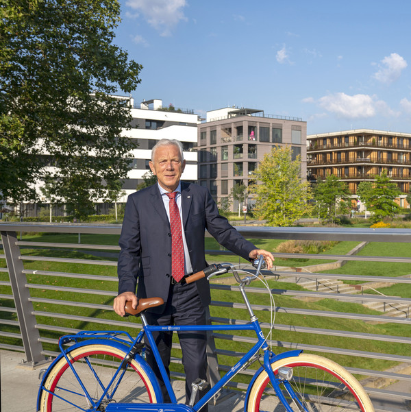 Oberbürgermeister Harry Mergel stehend mit Fahrrad im Stadtquartier Neckarbogen.