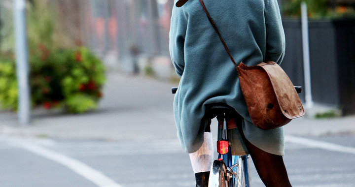 Das Foto zeigt eine Frau mit Hut und Umhängetasche auf einem Fahrrad.
